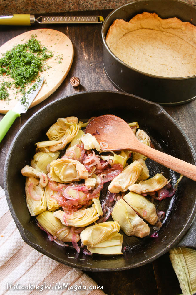 cooked artichoke hearts and red onion in a skillet